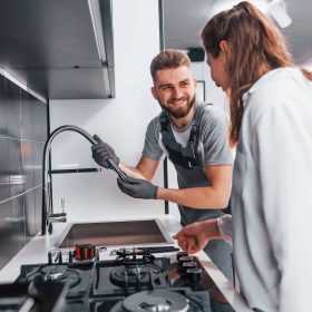 young-professional-plumber-in-grey-uniform-shows-results-of-work-for-housewife-on-the-kitchen.jpg